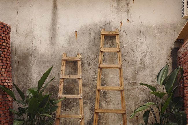 Two ladders side by side stnading against a wall
